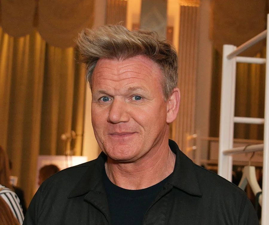 Renowned chef smiling at an indoor event with elegant décor in the background.