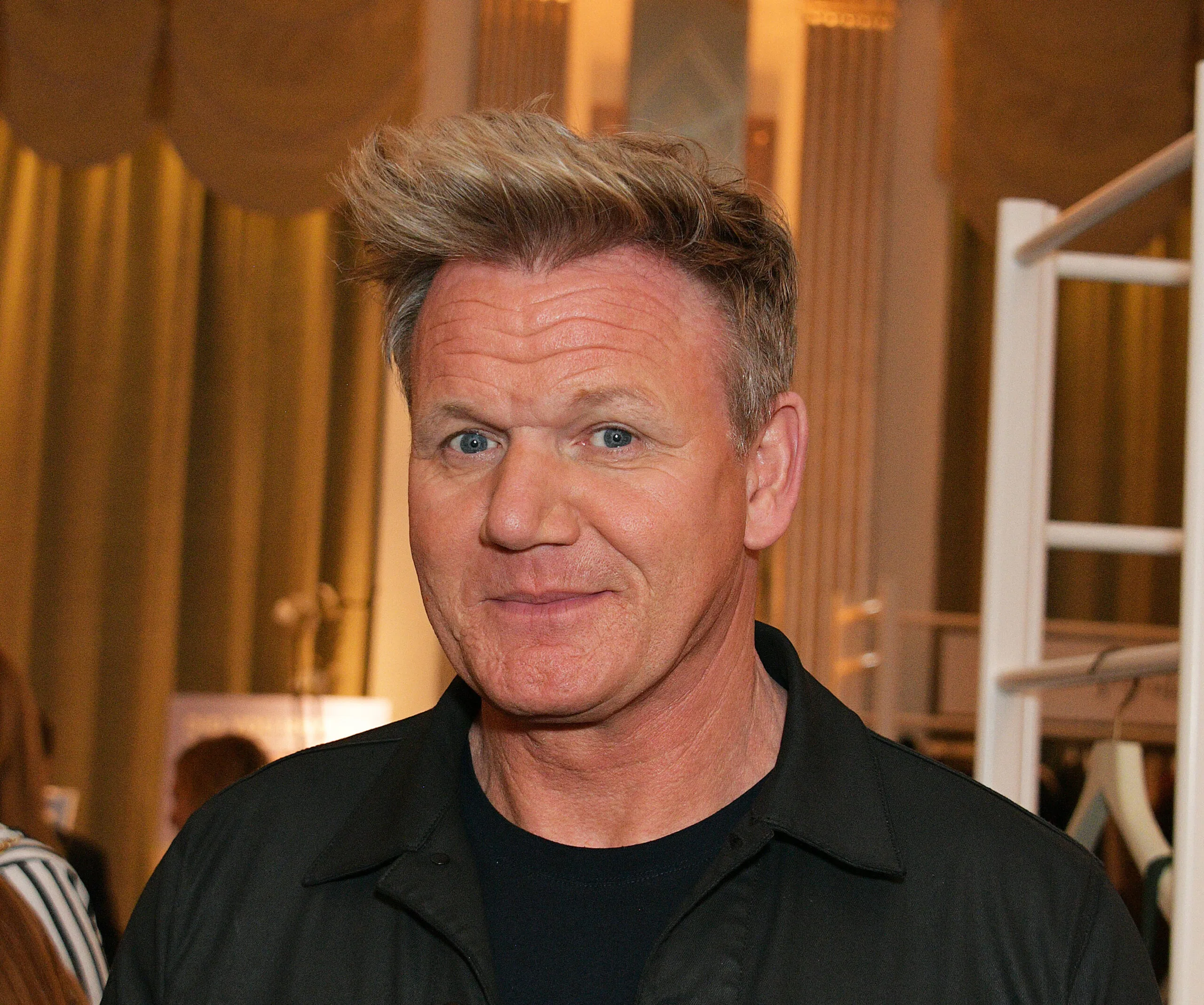 Renowned chef smiling at an indoor event with elegant décor in the background.
