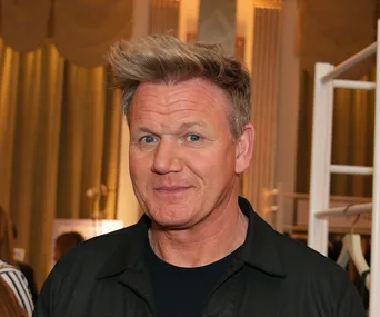 Renowned chef smiling at an indoor event with elegant décor in the background.