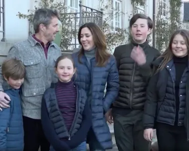 A family of six in winter clothing smiles and stands together outdoors.