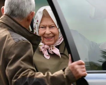 A smiling elderly woman in a headscarf is greeted by a man holding a car door open for her.