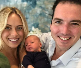 A smiling couple holding their newborn baby indoors.