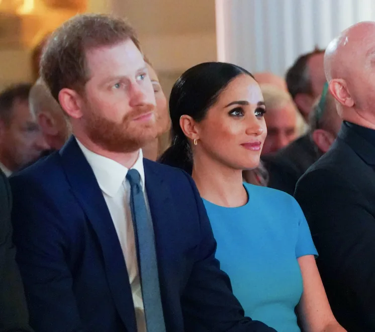 Couple sitting at an event, the man in a suit and the woman in a blue dress, looking attentively forward.