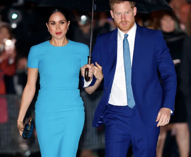 Prince Harry and Meghan Markle walking under an umbrella, dressed in coordinated blue outfits.