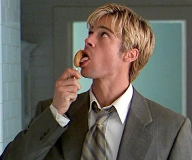A person in a suit licking a spoon, looking upwards.