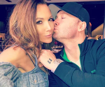 Couple sitting together as the man kisses the woman's cheek in a close-up selfie.
