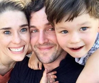 A smiling family of three posing closely together outdoors.