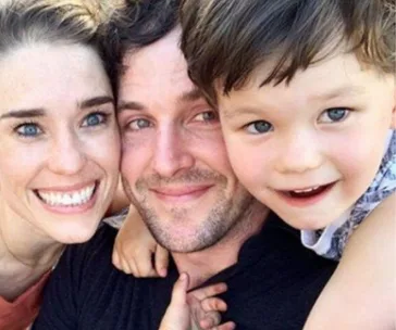 A smiling family of three posing closely together outdoors.