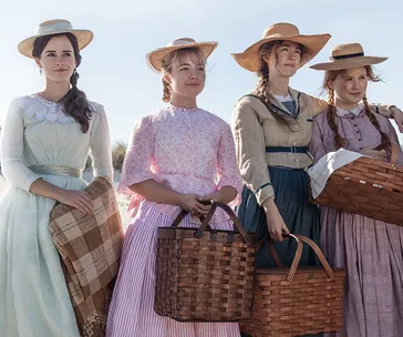 Four women in period dresses and straw hats hold baskets, standing outdoors with a sunny sky.