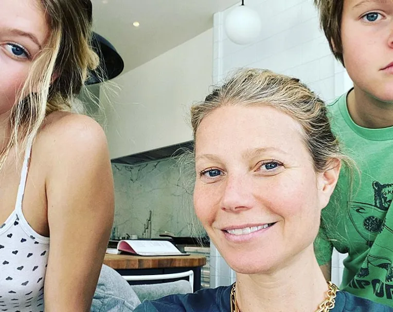 Family selfie with smiling woman and two kids in a modern kitchen setting.