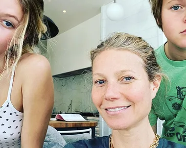 Family selfie with smiling woman and two kids in a modern kitchen setting.