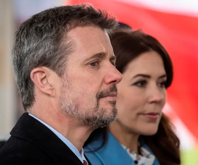 A man and woman in formal attire, standing together at an event, with a red and white backdrop.