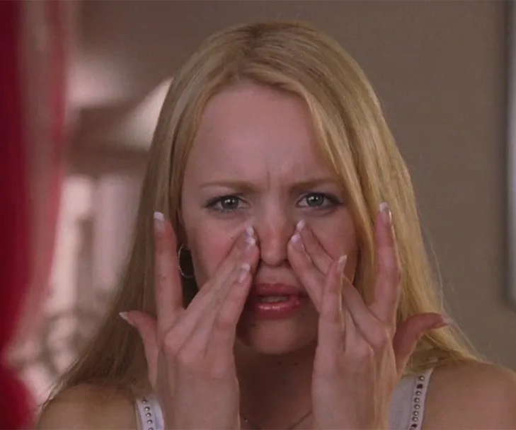 A person pinching their nose with both hands, appearing to examine their skin closely.