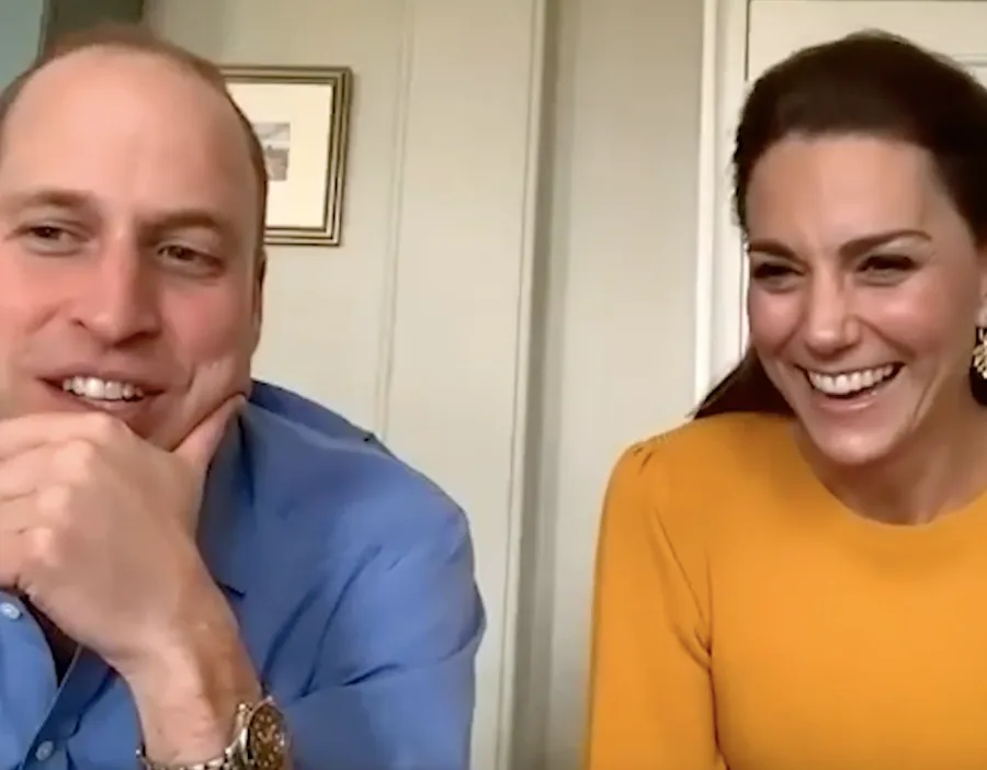 Two people smiling during a video call, seated side by side in a light-colored room.