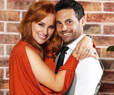 ```
A couple smiling and embracing, with the woman in an orange top and the man in a vest and tie.
```