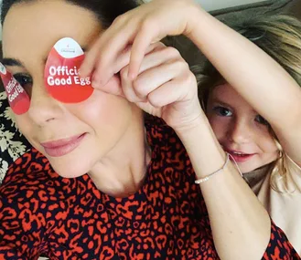Mom and daughter pose playfully with "Official Good Egg" stickers on their eyes, wearing a red patterned shirt.