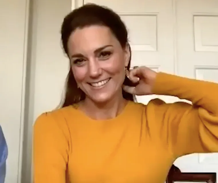 A woman in an orange jumper smiles during a video call.