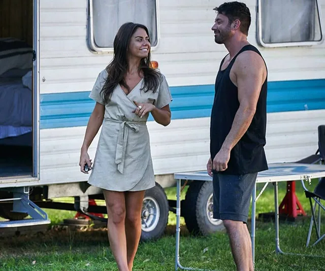 Two characters from "Home and Away" talking outside a trailer, one in a dress, the other in a tank top and shorts.