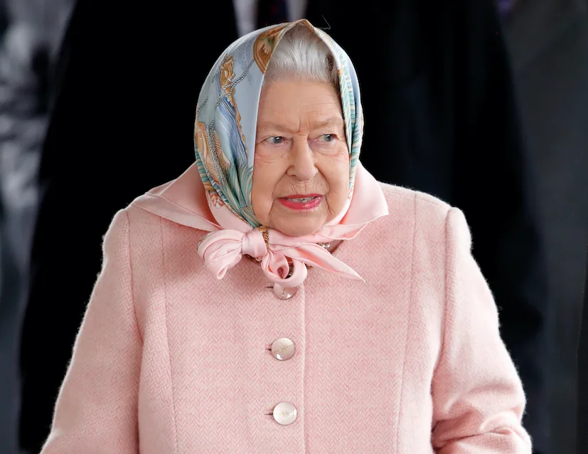 Elderly woman in a pink coat and patterned headscarf outdoors.