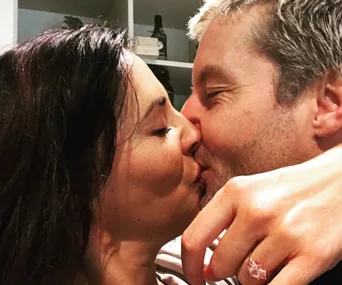 A couple shares a kiss, close up showing an engagement ring on the woman's finger.