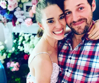 Couple embracing and smiling in front of a floral background.