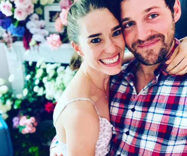 Couple embracing and smiling in front of a floral background.
