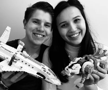 Young couple smiling, holding LEGO spaceship and dinosaur models.