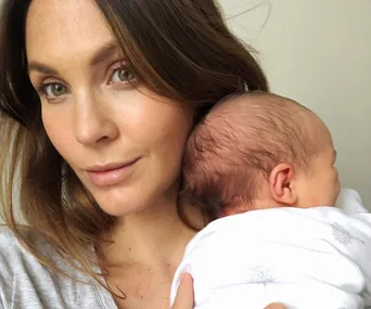 Woman holding a baby against her shoulder, with a gentle expression.