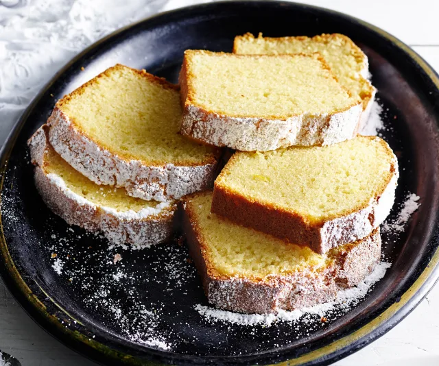 Slices of pound cake dusted with powdered sugar on a black plate.