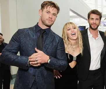Three people posing together at an indoor event, all dressed in formal attire.