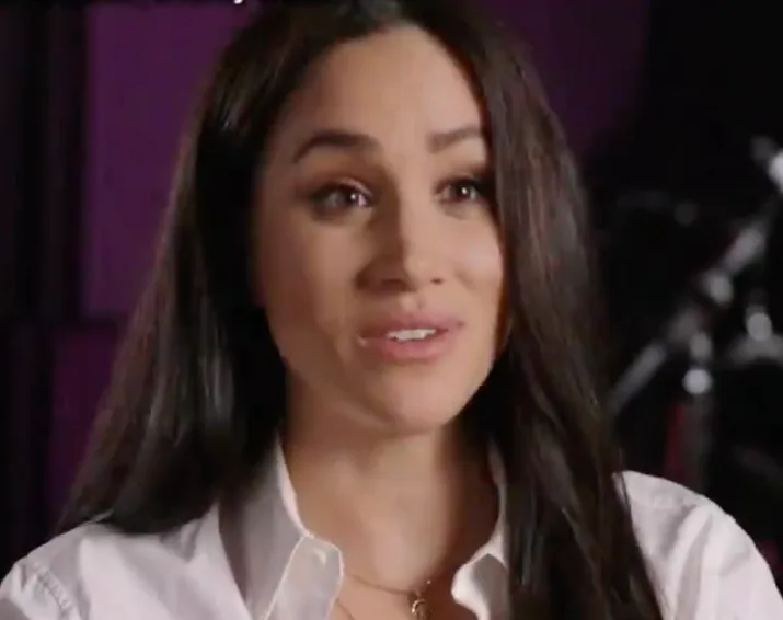 A woman with long dark hair in a white blouse speaking, possibly during an interview.
