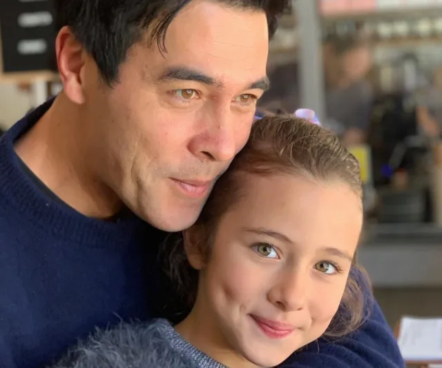Man and young girl smiling together, embracing closely, both wearing blue.