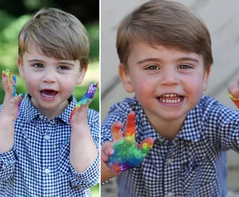 Young child with brown hair, smiling and showing colorful painted hands, wearing a checkered shirt outdoors.