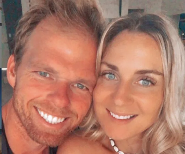 A smiling couple taking a close-up selfie indoors, both have light-colored hair.