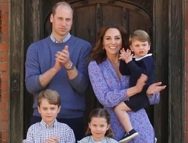 A family of five clapping, standing outside a door; parents with three children, one being held.