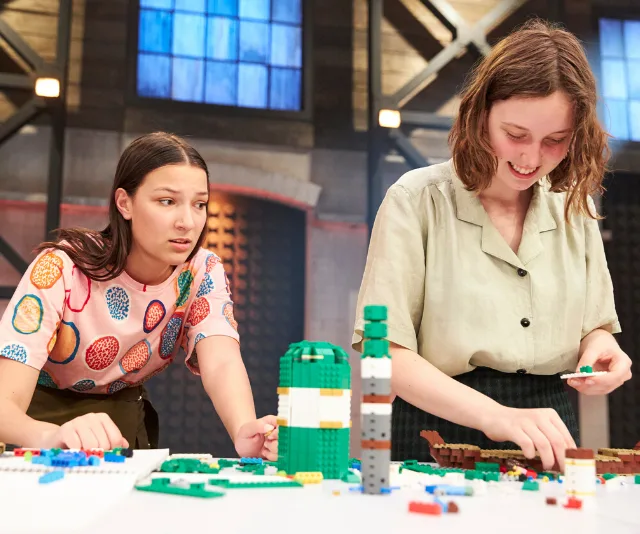 Two contestants on LEGO Masters Australia building colorful LEGO models on a competition table.