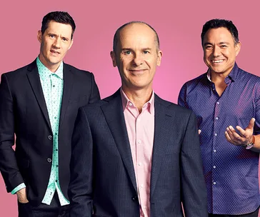Three men in suits stand against a pink background, smiling at the camera.