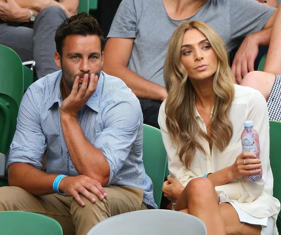 A couple sitting closely in stadium seats; one person holding a water bottle.
