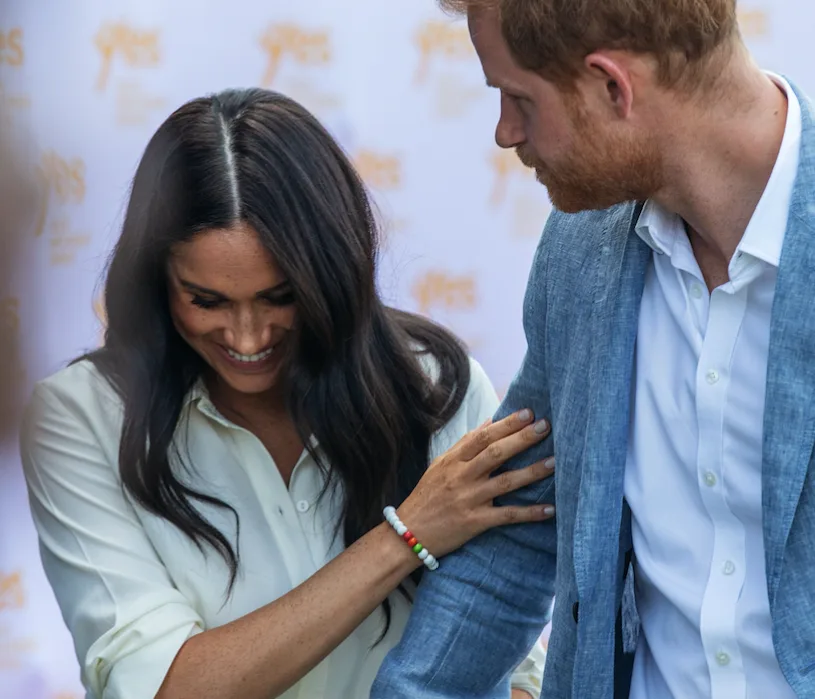 Couple in conversation, smiling and holding each other's arms, with a blurred background.