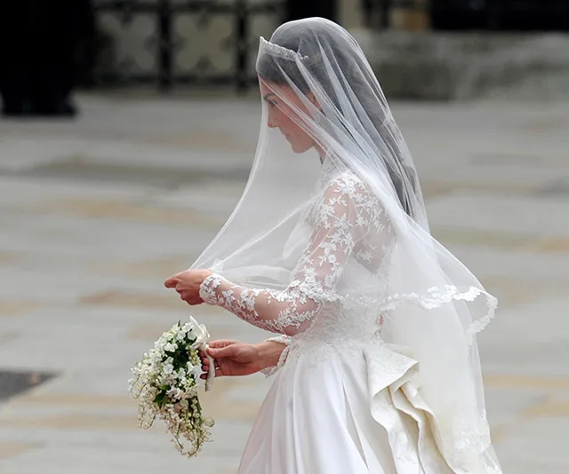 Bride in lace wedding dress and veil holding bouquet.