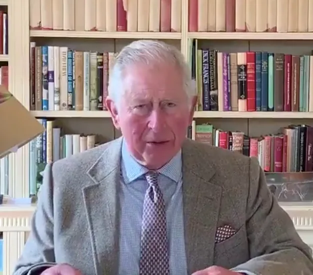 Man in a suit speaking in front of a bookshelf filled with books.