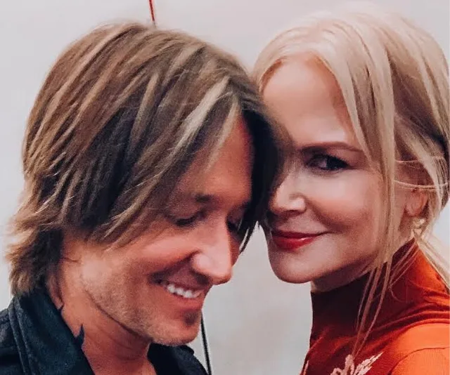 A couple smiling closely together, with the woman wearing a red top and both having light-colored hair.