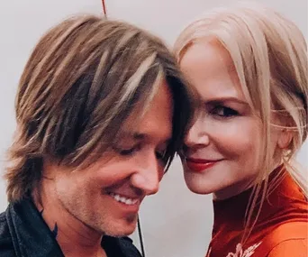 A couple smiling closely together, with the woman wearing a red top and both having light-colored hair.