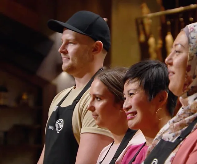 Contestants standing together on MasterChef, wearing aprons and attentively facing forward.