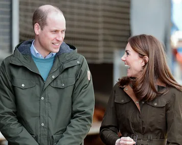 A man and woman smiling and talking, both wearing casual jackets outdoors.