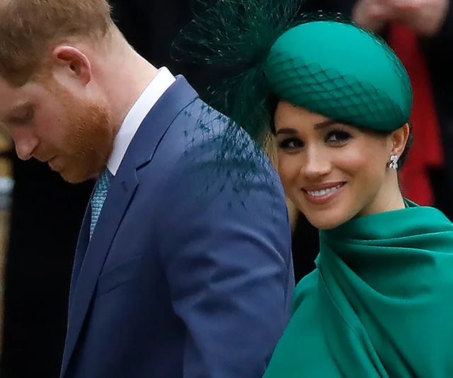 A man in a suit and a woman in a green outfit with a matching hat, smiling at a formal event.