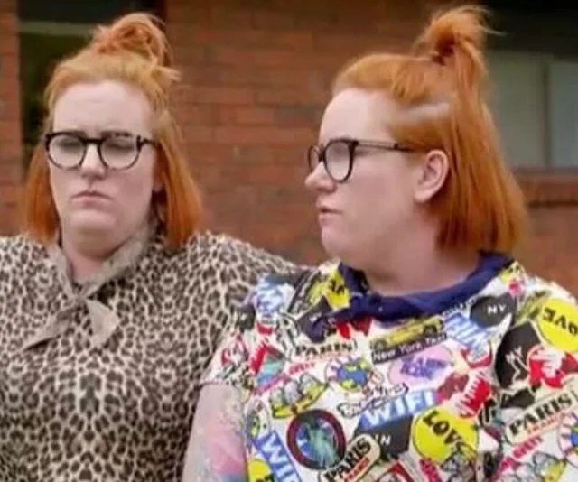 Two people with red hair and glasses sit outdoors, one in leopard print, the other in a colorful patterned shirt.