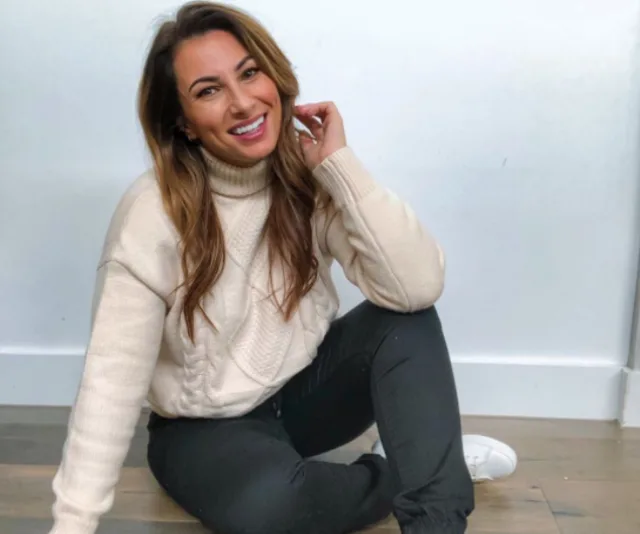 Person sitting on the floor in a cozy outfit, smiling warmly at the camera.