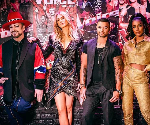 Judges from "The Voice" pose in colorful and glamorous outfits against a backdrop of show posters.