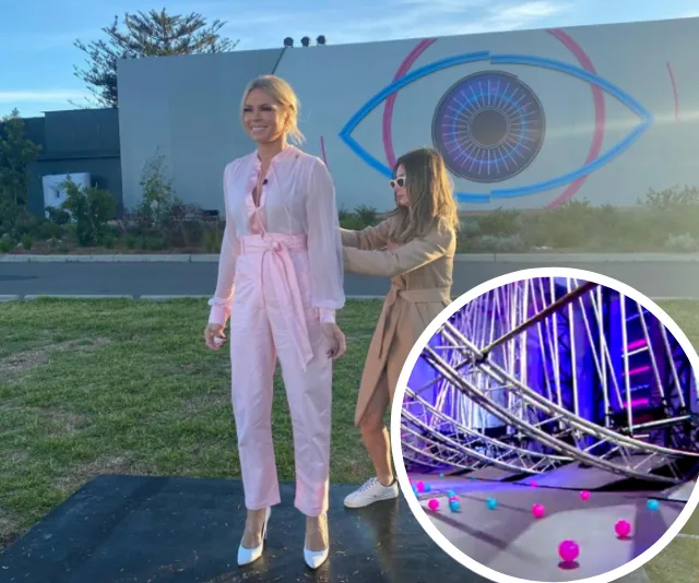 Two women are outside with a large Big Brother eye symbol on the wall; one is adjusting the other's outfit. Small inset of a game setup with spheres.
